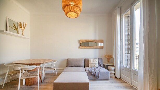 Una sala de estar moderna con una mesa redonda de madera, un sofá gris y un amplio ventanal con cortinas blancas.