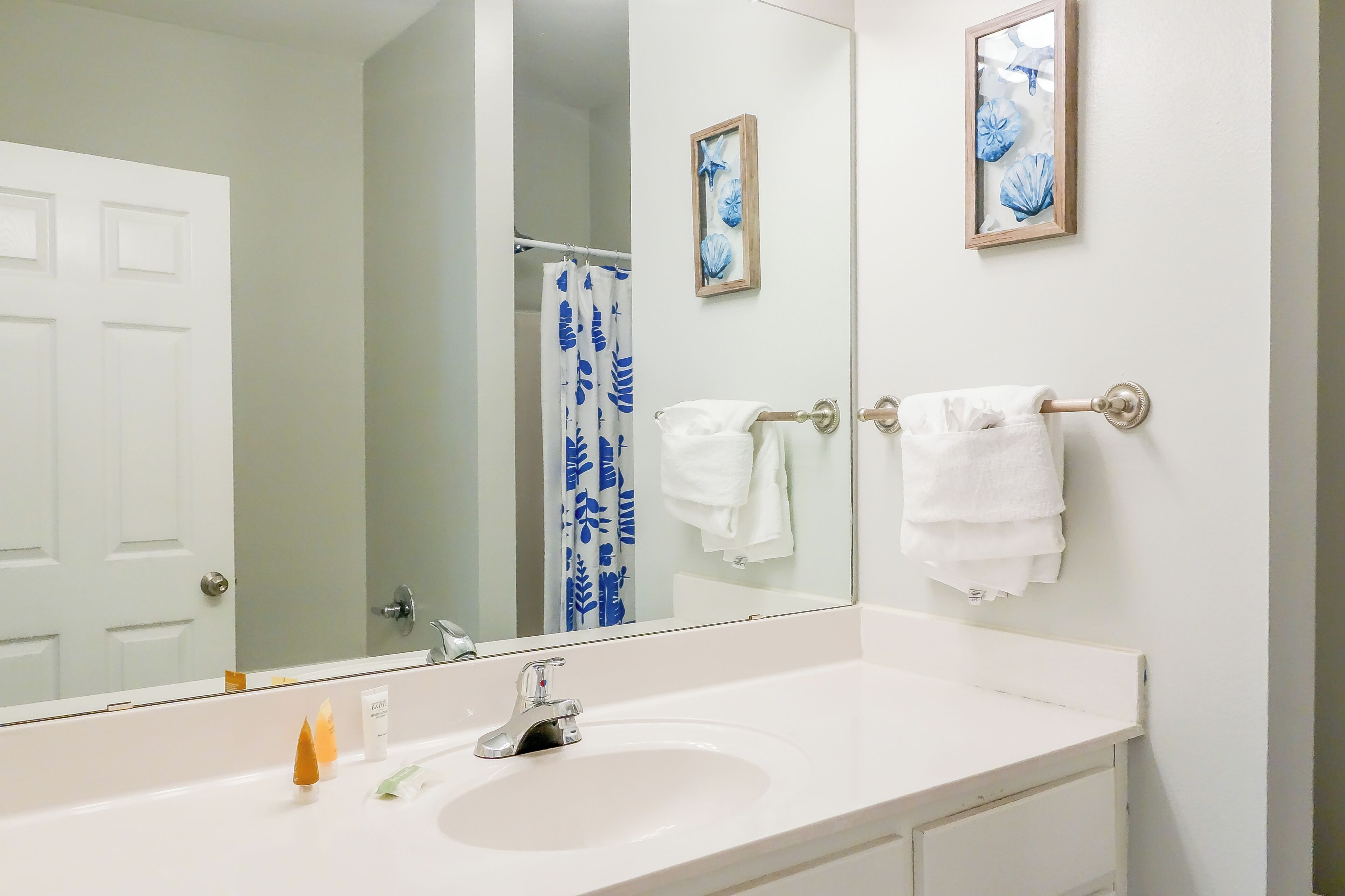 A bathroom with a white sink, a mirror, and two framed pictures on the wall.