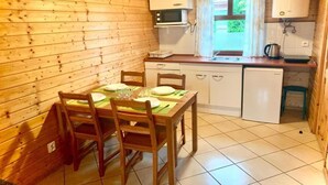 A wooden cabin with a dining area, a kitchen with a microwave and sink, and a window with curtains. - Comfortable holiday homes, close to the beach (Sarbinowo)