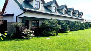 A two-story house with a covered porch, surrounded by a well-maintained lawn and various shrubs. - Comfortable holiday homes, close to the beach (Sarbinowo)