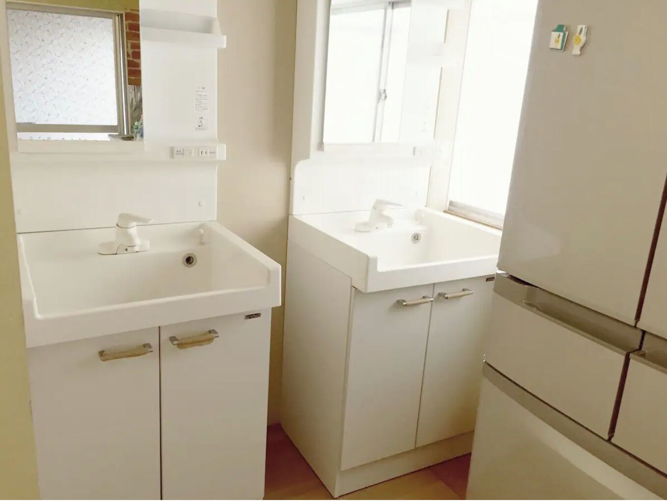 A small, clean bathroom with two sinks, a mirror, and a window.