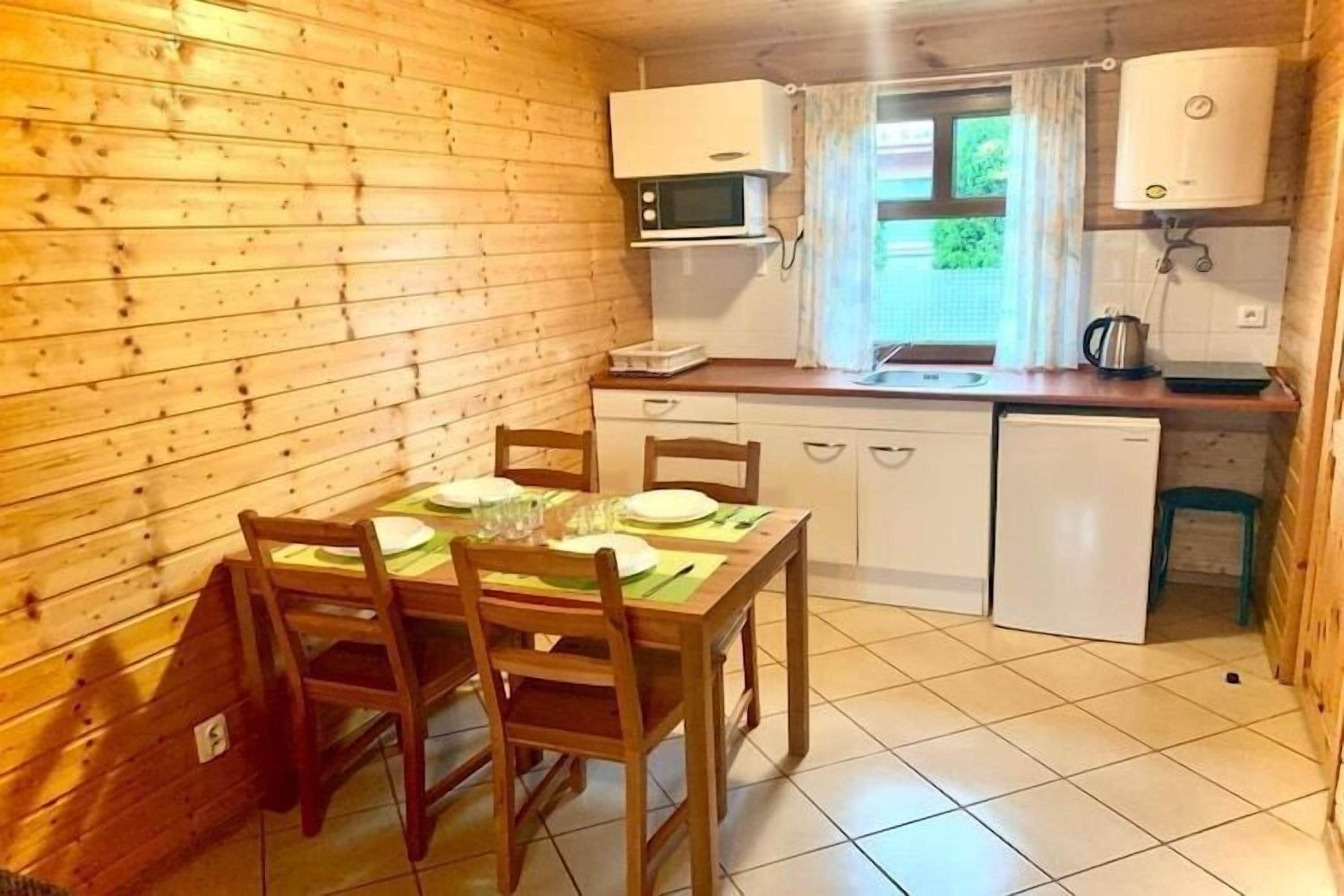 A wooden cabin with a dining table set for four, a microwave, a sink, and a small refrigerator.