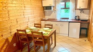 Eine Holzhütte mit einem Esstisch, der für vier Personen gedeckt ist, einer Mikrowelle, einem Spülbecken und einem kleinen Kühlschrank.