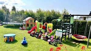Ein Spielplatz mit verschiedenen Spielgeräten, einer Hüpfburg und einem kleinen Haus.