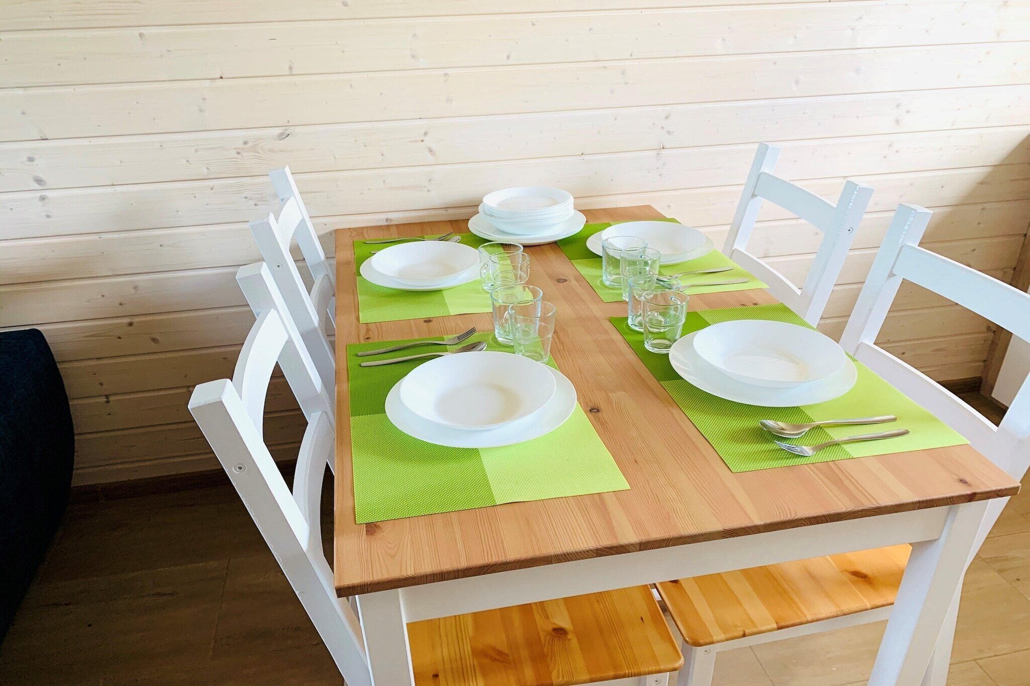 A wooden dining table with white chairs, set with plates, glasses, and cutlery.