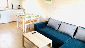 Een ruimtelijk ingerichte leefruimte met een bank, een eettafel met stoelen, een klein keukentje en een enkel bed.