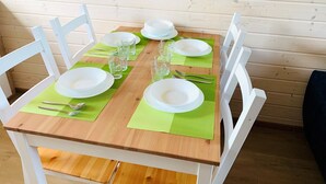 Een eettafel gedekt met witte borden, glazen en bestek, omringd door witte stoelen, tegen een houten wandpaneel.