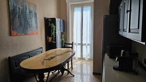 Uma área de refeições com uma mesa de mármore, cadeiras pretas, um quadro na parede e uma cozinha com armários e eletrodomésticos.