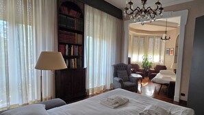 Quarto de hotel com cama, estante, candelabro e área de jantar.