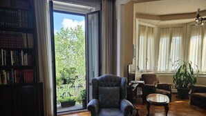 Uma sala de estar com uma poltrona azul, uma mesa de centro de madeira e uma estante repleta de livros.