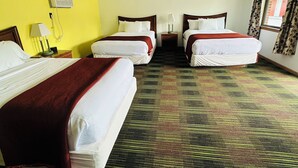 Une chambre d’hôtel avec trois lits, une moquette à motifs et un mur jaune.