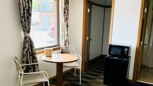 Une petite pièce avec une table ronde, deux chaises blanches, un four à micro-ondes et une porte donnant sur une autre pièce.