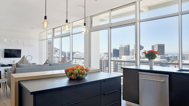 Una cocina moderna con un amplio ventanal, un cuenco de fruta sobre la encimera y vistas a la ciudad.