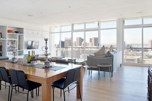 A modern living space with a dining area, a sofa, and a city view through large windows.