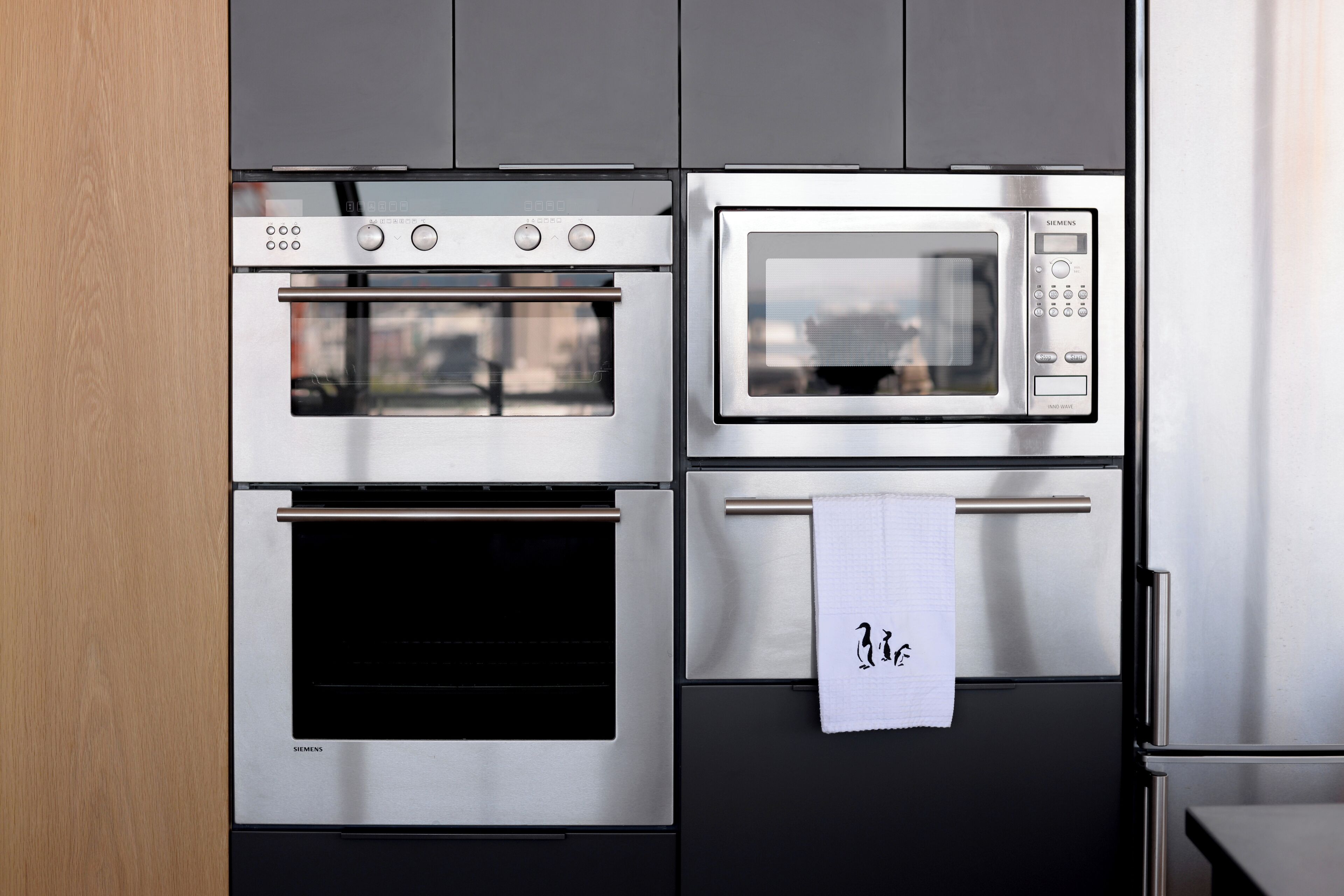A kitchen with a built-in oven, microwave, and a stainless steel refrigerator.