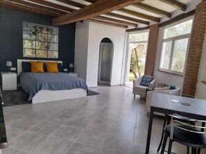 Ein geräumiges Schlafzimmer mit einem großen Bett, einem Schreibtisch und einem Stuhl. Ein Fenster bietet Blick auf Bäume und eine Ziegelwand.