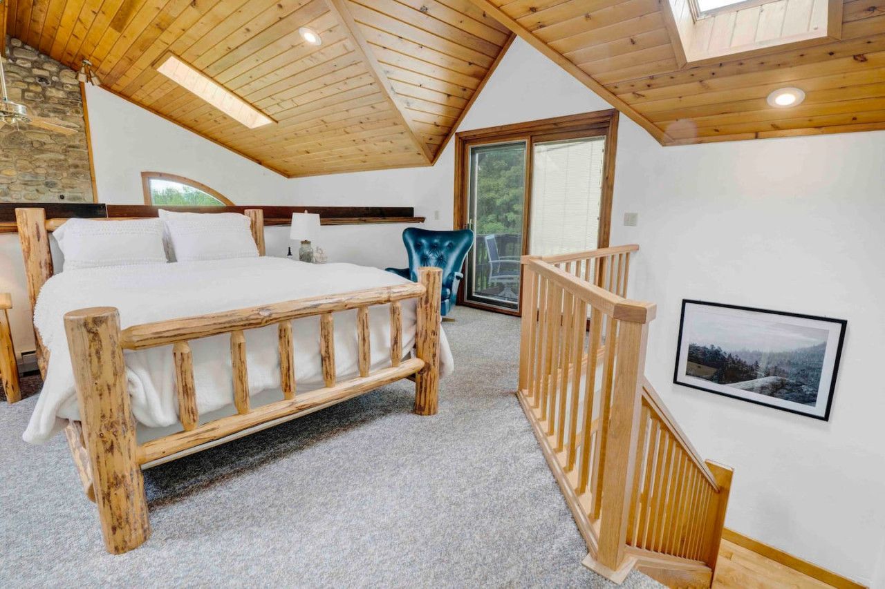 Une chambre avec un lit en bois, une chaise bleue, un escalier en bois et un tableau encadré au mur.