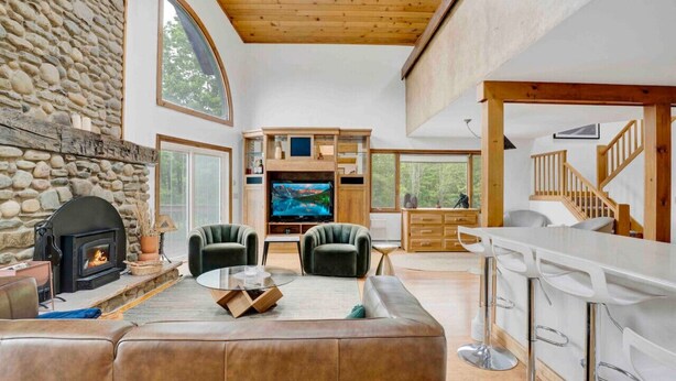 A spacious living area with a stone fireplace, comfortable seating, a flat-screen TV, and a kitchen with bar stools.