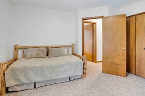 Une chambre à coucher avec une tête de lit en bois, un lit recouvert d’une courtepointe beige et un sol moquetté.