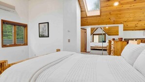 A bedroom with a large bed, wooden ceiling, and a skylight.