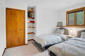 A bedroom with two beds, a wooden wardrobe, shelves with items, a window, and a nightstand with a lamp. - Poolside Paradise on Plum Creek (Ellicottville)