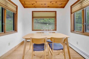 Comedor con mesa y sillas de madera, ventanas amplias con persianas y vistas a zonas verdes.