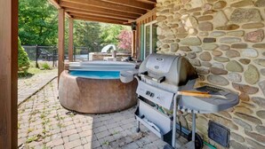 An outdoor patio with a stone wall, a hot tub, and a barbecue grill.