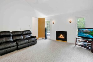 A living room with a black leather sofa, a fireplace, a TV on a stand, and a door leading to another room.