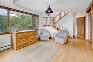 Un interior moderno con un aparador de madera, dos sillones grises, un tapete redondo y una escalera con barandillas de madera.