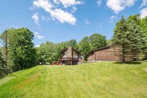 Un grand chalet rustique doté d’une cheminée en pierre, d’un porche abrité et d’une pelouse bien entretenue.