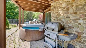Une terrasse extérieure avec un mur en pierre, un jacuzzi et un barbecue.