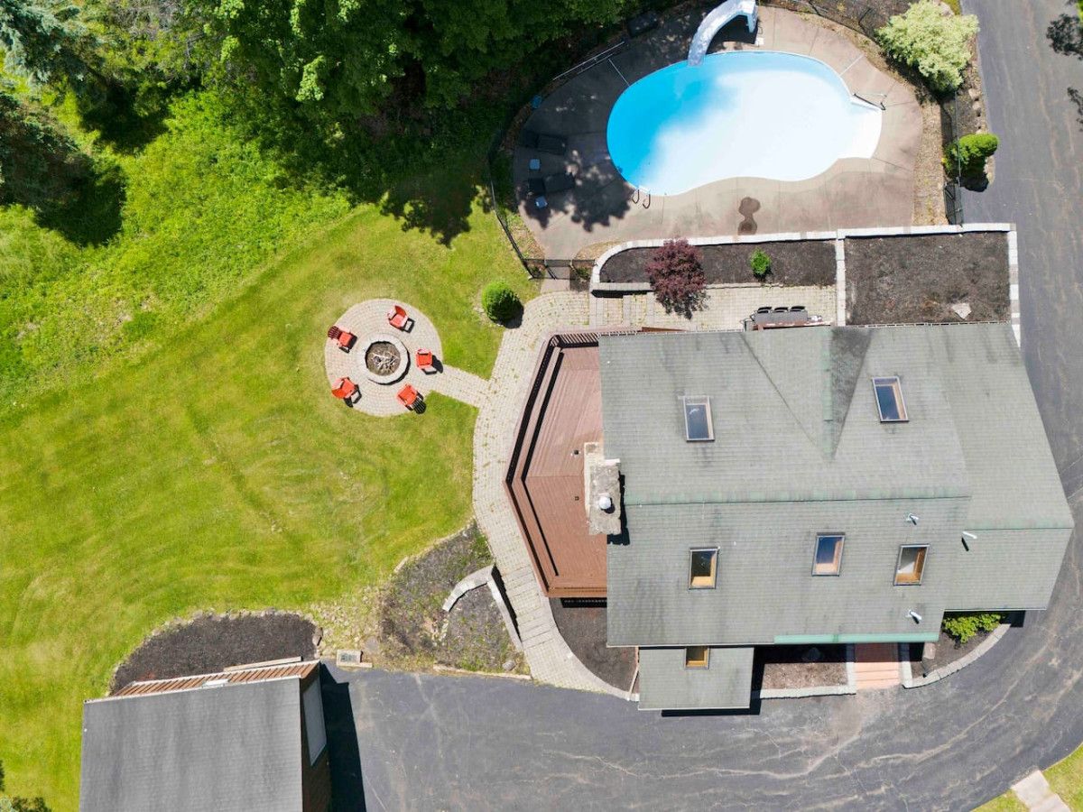 Ein Luftbild eines Anwesens mit Swimmingpool, einer Terrasse mit Gartenmöbeln und einem Haus mit geneigten Dächern.