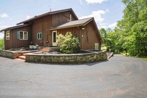 A two-story wooden house with a front porch, a small garden, and a driveway.