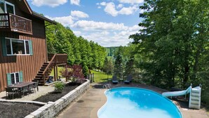 A backyard with a swimming pool, a deck, and a slide.