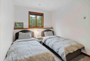 A bedroom with two single beds, a window, a nightstand, and a wall-mounted painting.
