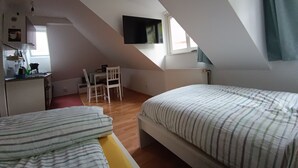 Ein Schlafzimmer mit zwei Betten, einem Schreibtisch und einem an der Wand befestigten Fernseher.
