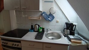 Eine Küche mit Herd, Spüle und verschiedenen Geräten. Oberhalb der Spüle befindet sich ein Holzregal und ein Handtuch hängt an der Wand.