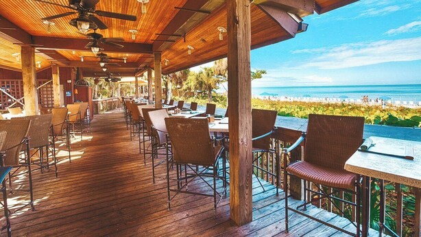 A wooden deck with tables and chairs, overlooking a beach. - LUXE, Beach, Hot Tub, Putt Putt, 2 Mstr Suites, 3 Kings, Hot Tub, Bunkbds, Pets (Naples)