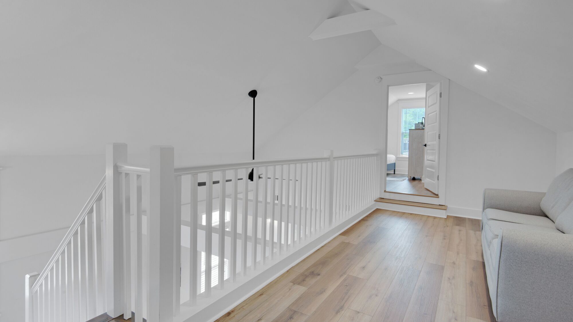 A spacious room with a white railing, a wooden floor, and a grey sofa.