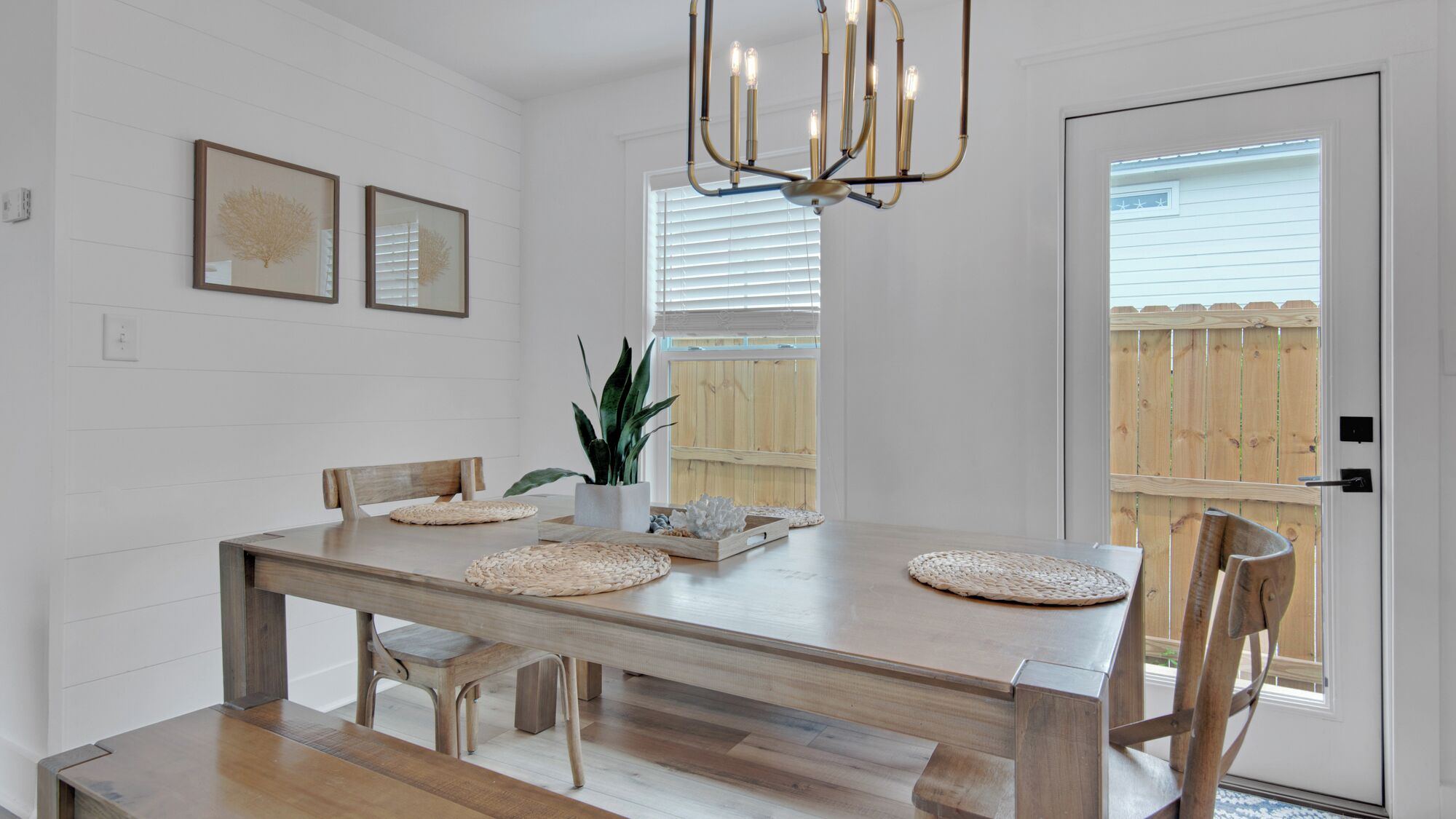A dining room with a wooden table, chairs, a chandelier, and framed artwork on the wall.