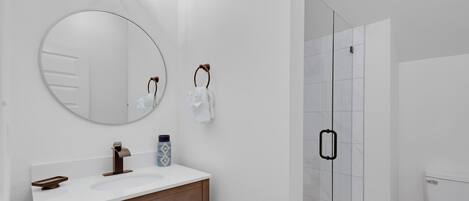 Ein modernes Badezimmer mit rundem Spiegel, weißem Waschtisch und einer Duschkabine aus Glas.