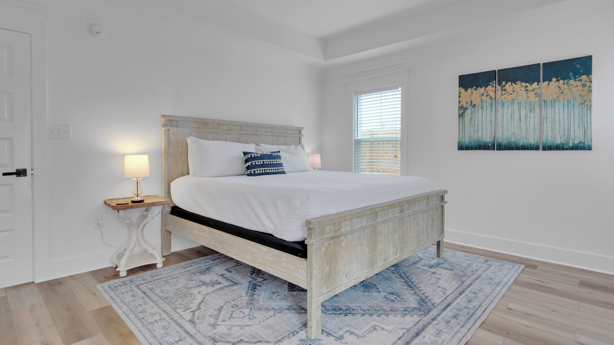 A bedroom with a bed, bedside tables, a rug, and a painting on the wall.