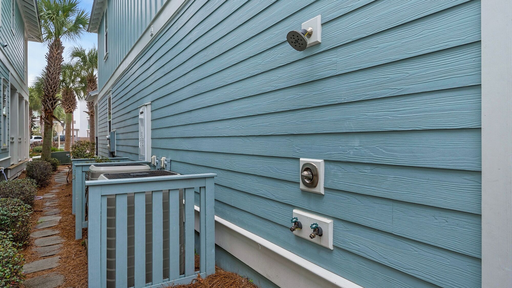 Fachada azul de un edificio con un pequeño porche, un grifo y una unidad de aire acondicionado.
