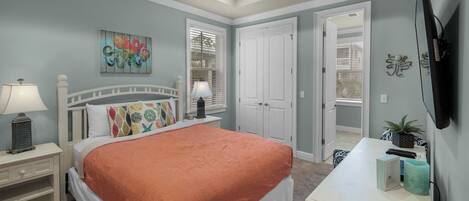 A bedroom with a bed, nightstands, a desk, a ceiling fan, and a door leading to another room.