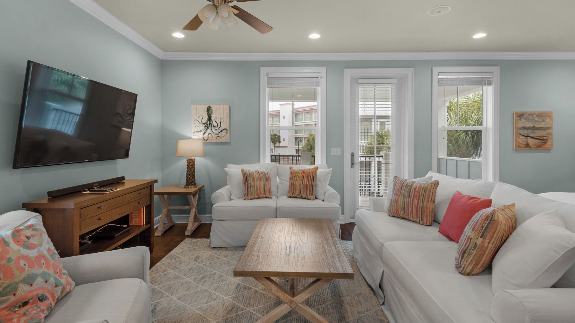 A living room with a TV, white sofas, a coffee table, and artwork on the walls.