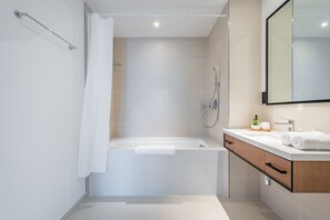 A modern bathroom with a bathtub, shower, and vanity with a mirror.