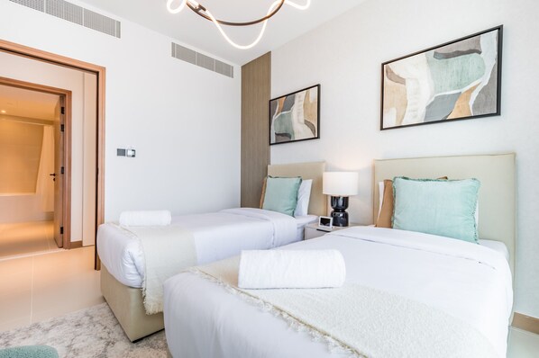 Habitación de hotel con dos camas, una puerta, una obra de arte colgada en la pared y una lámpara en el techo.