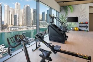 Ein Fitnessraum mit Rudergeräten, Laufbändern und Gymbällen mit Blick auf eine Marina und Boote.