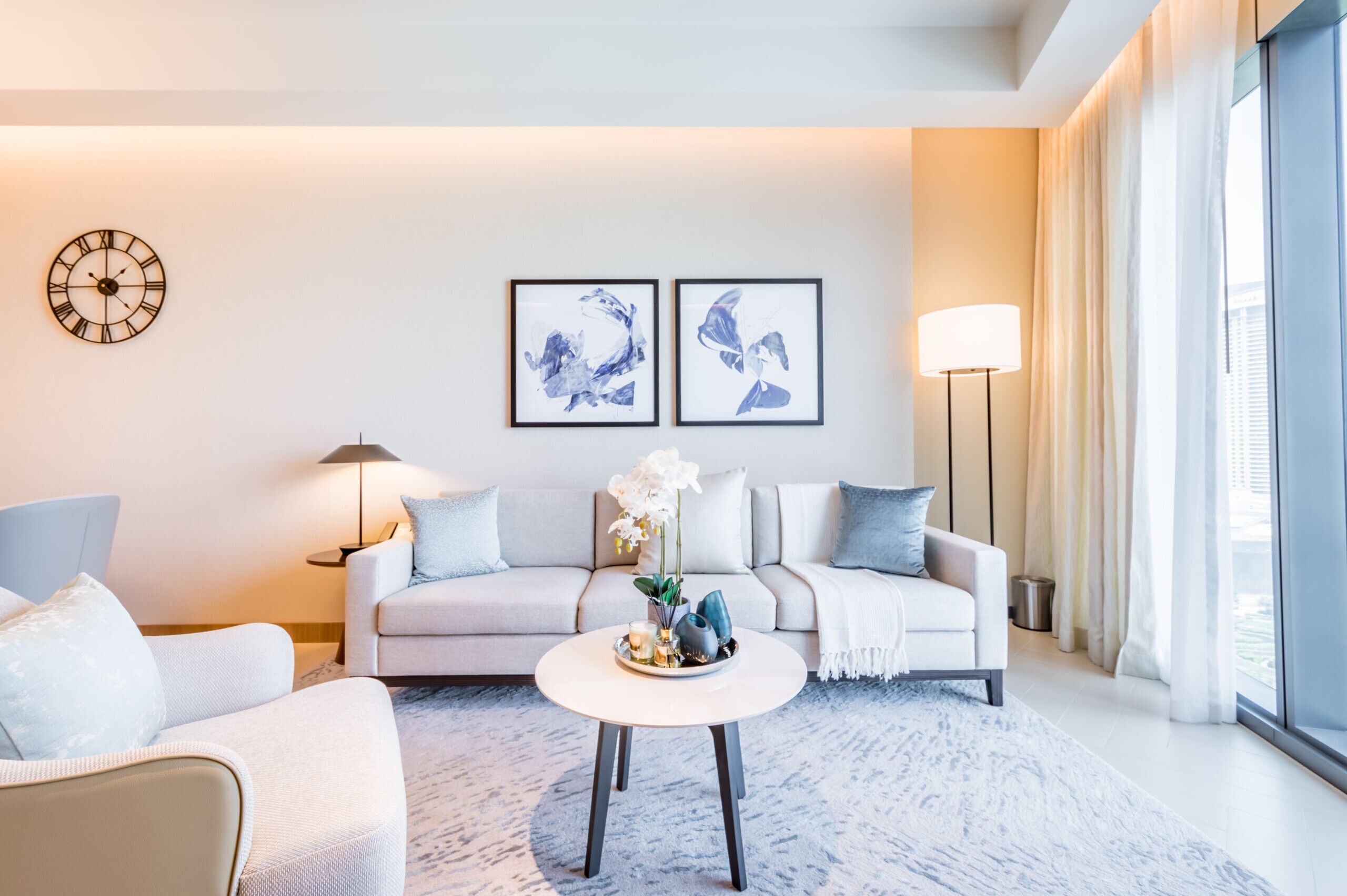 A modern living room with a sofa, a coffee table, a clock, and two framed artworks on the wall.