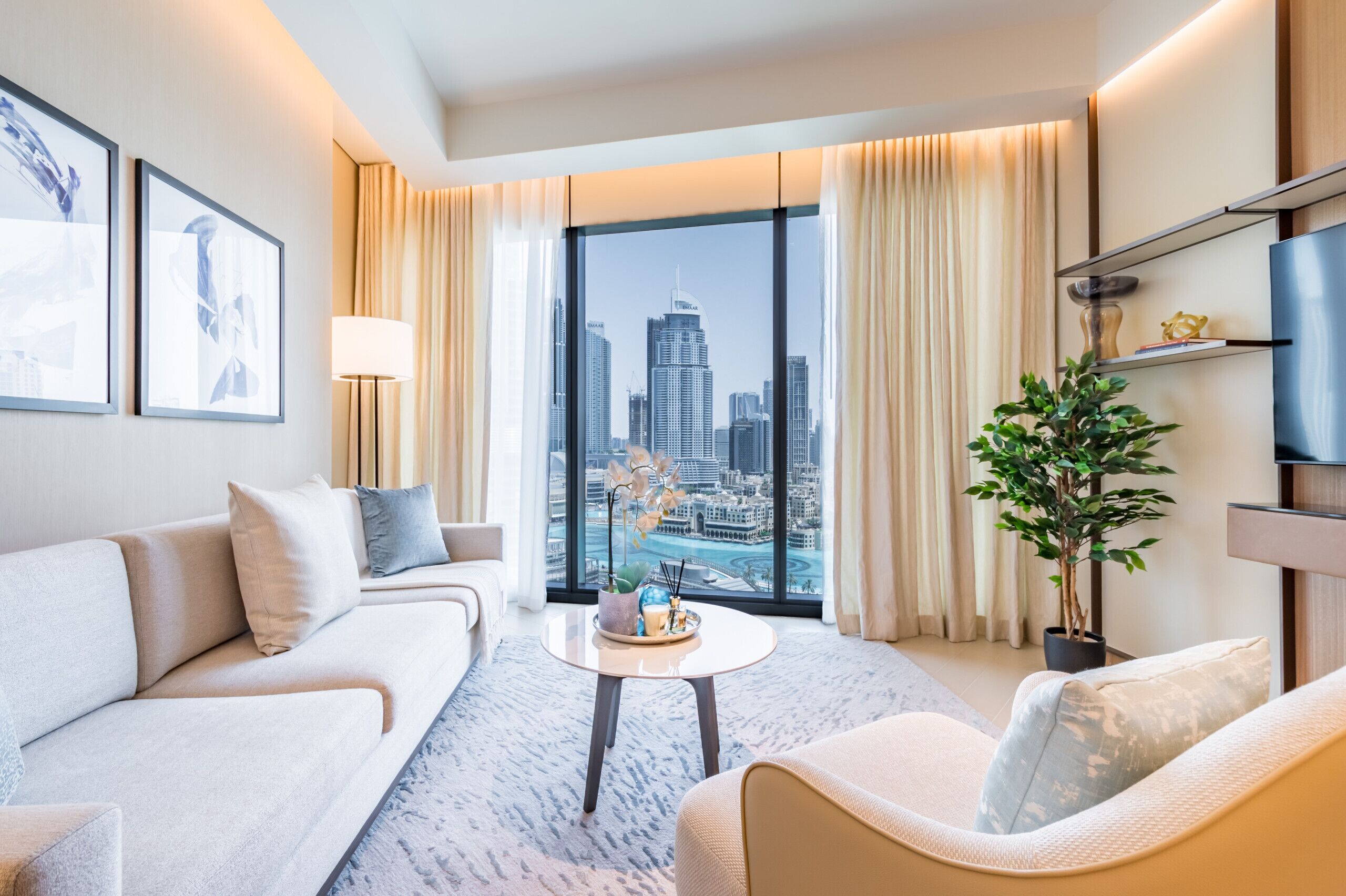 Een moderne hotelkamer met een groot raam met uitzicht op de stad, een bank, een bijzettafeltje en een potplant.
